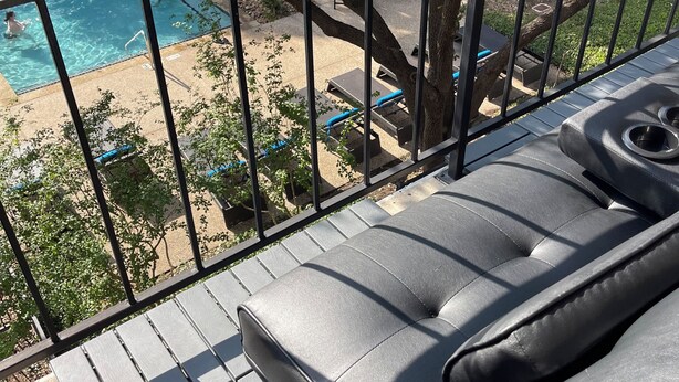 Un balcón con vista a la piscina, mobiliario exterior y barandilla de metal.