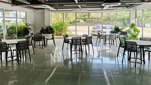 A spacious indoor area with tables and chairs arranged for dining, large windows offering a view of the outside, and visible ceiling pipes and lighting fixtures. - Full apartment Pto Azul Club House Come and Rest (Ricaurte)
