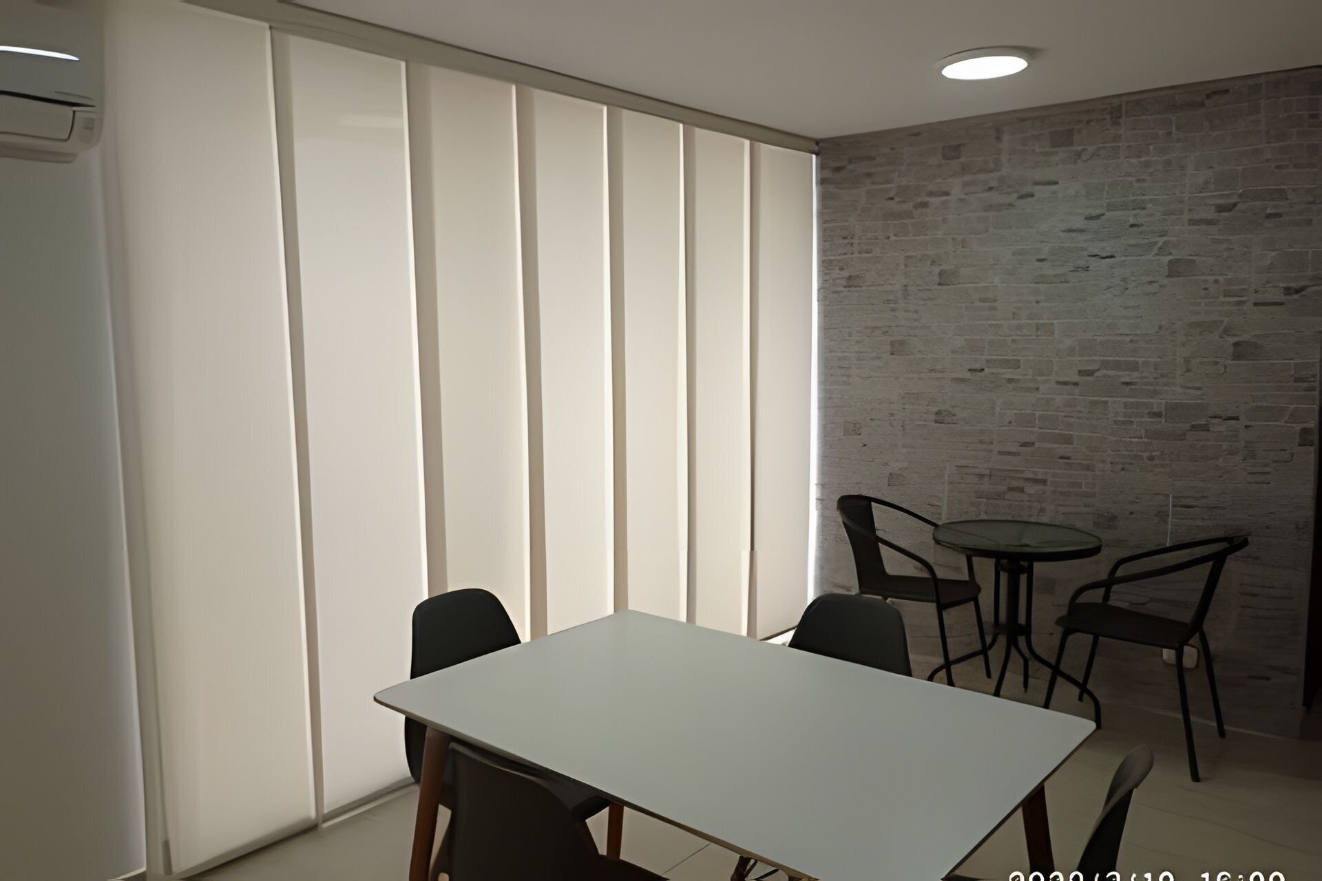 Een vergaderruimte met een witte tafel, zwarte stoelen, een tafel met glazen blad en een bakstenen muur.