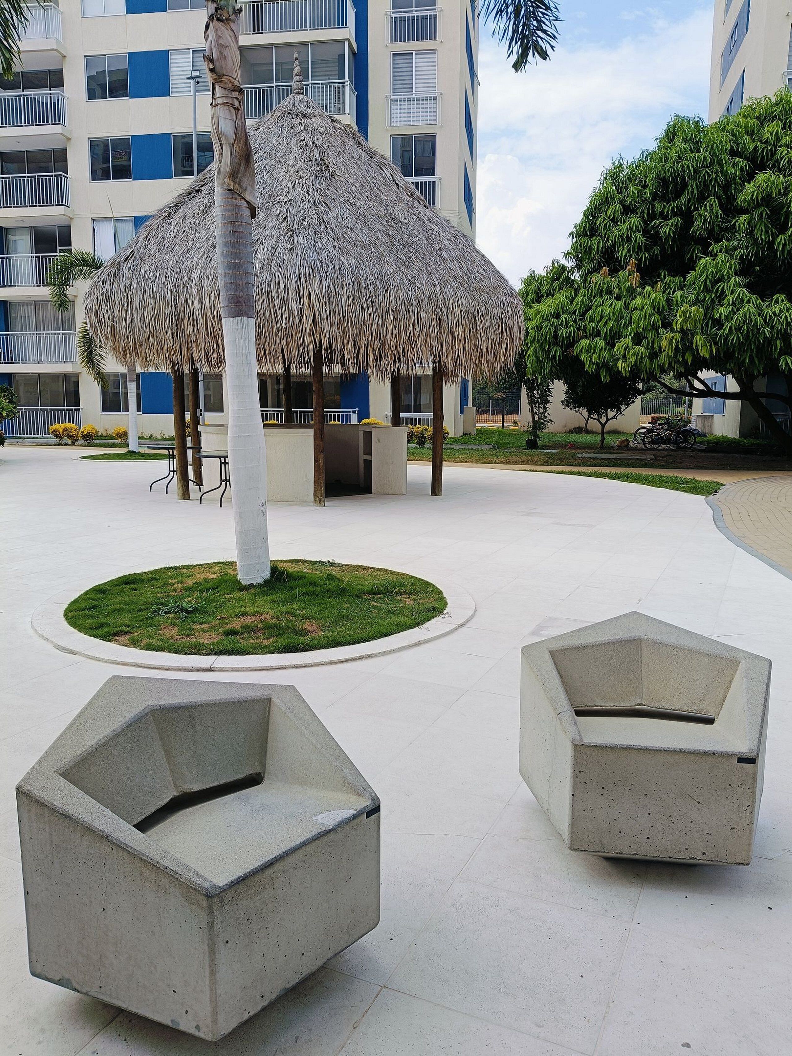 A modern outdoor area with a thatched structure, concrete seating, and a well-maintained lawn.