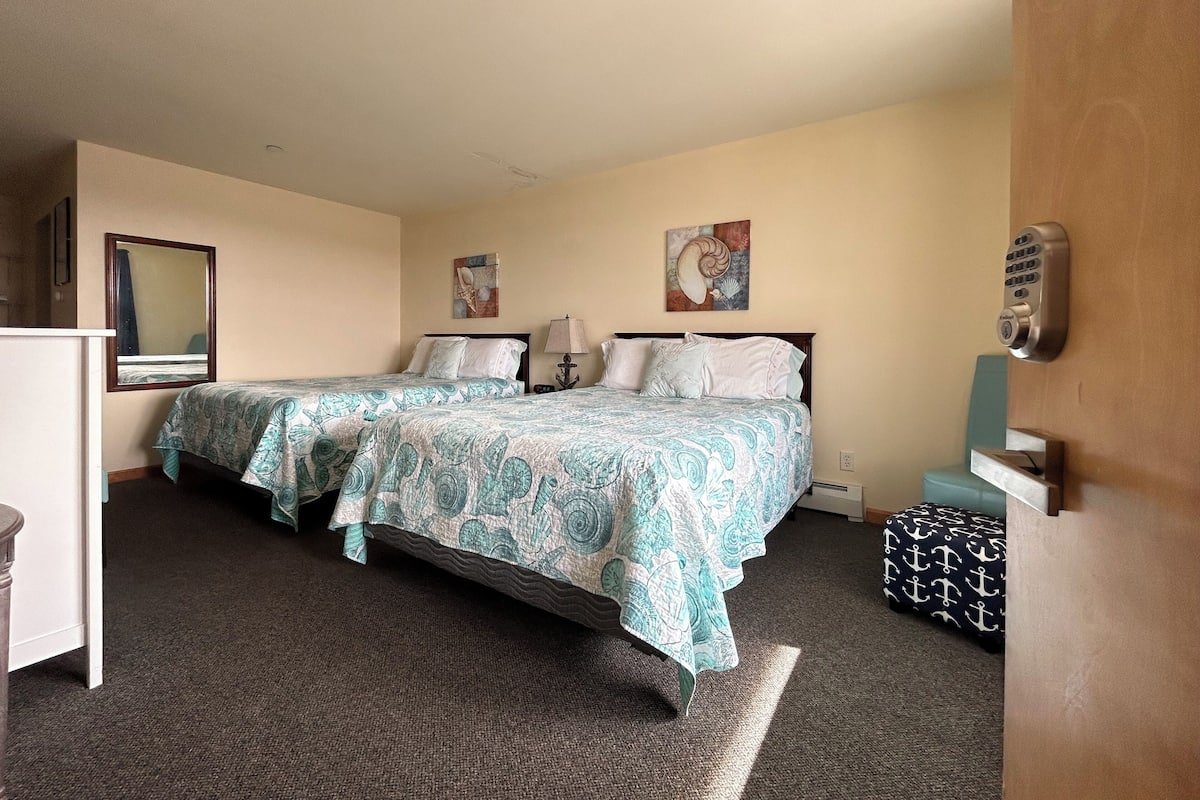 A hotel room with two beds, a desk, a mirror, and artwork on the walls.