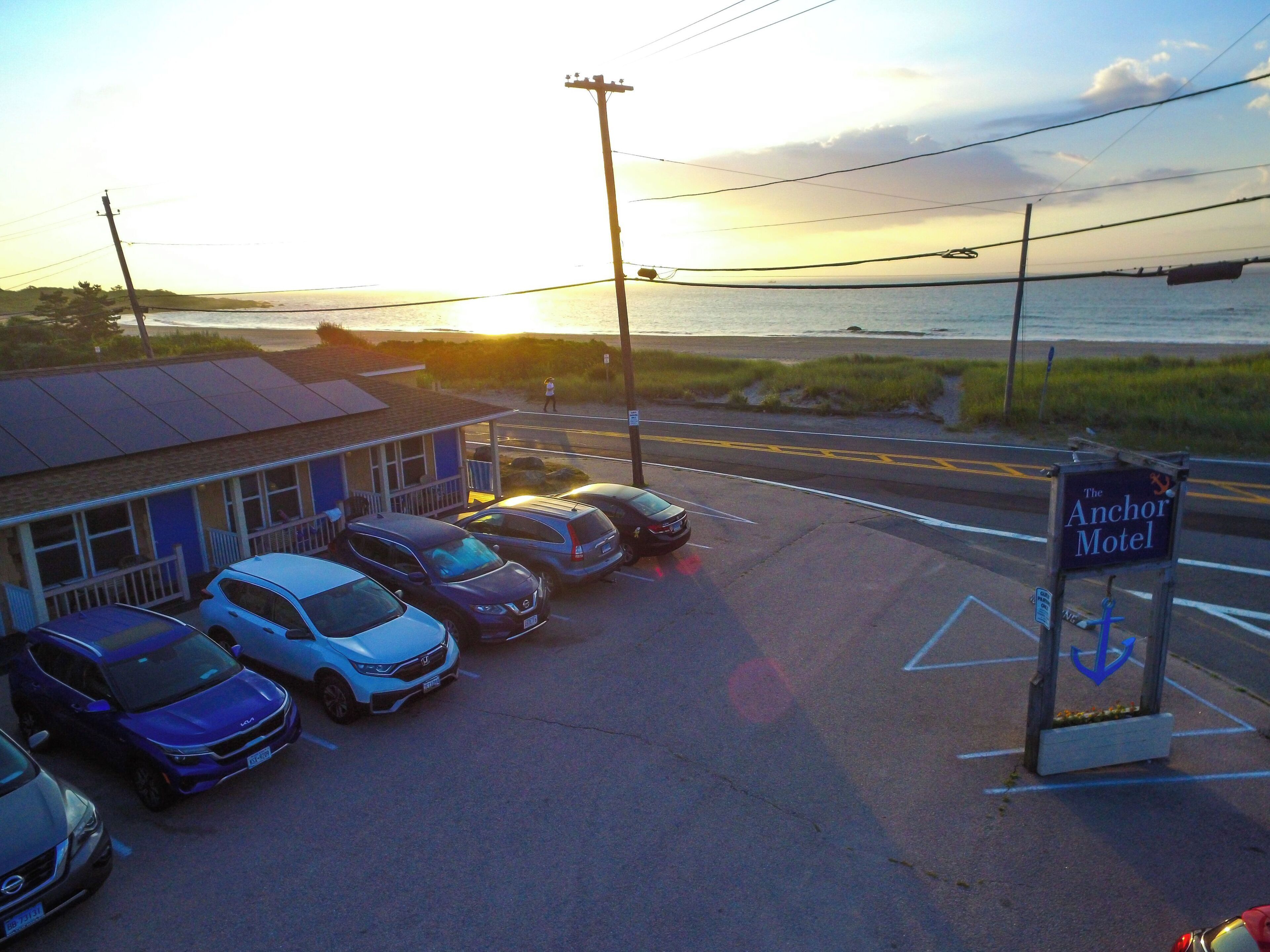 A motel with a signboard, parked cars, and a view of the sea.