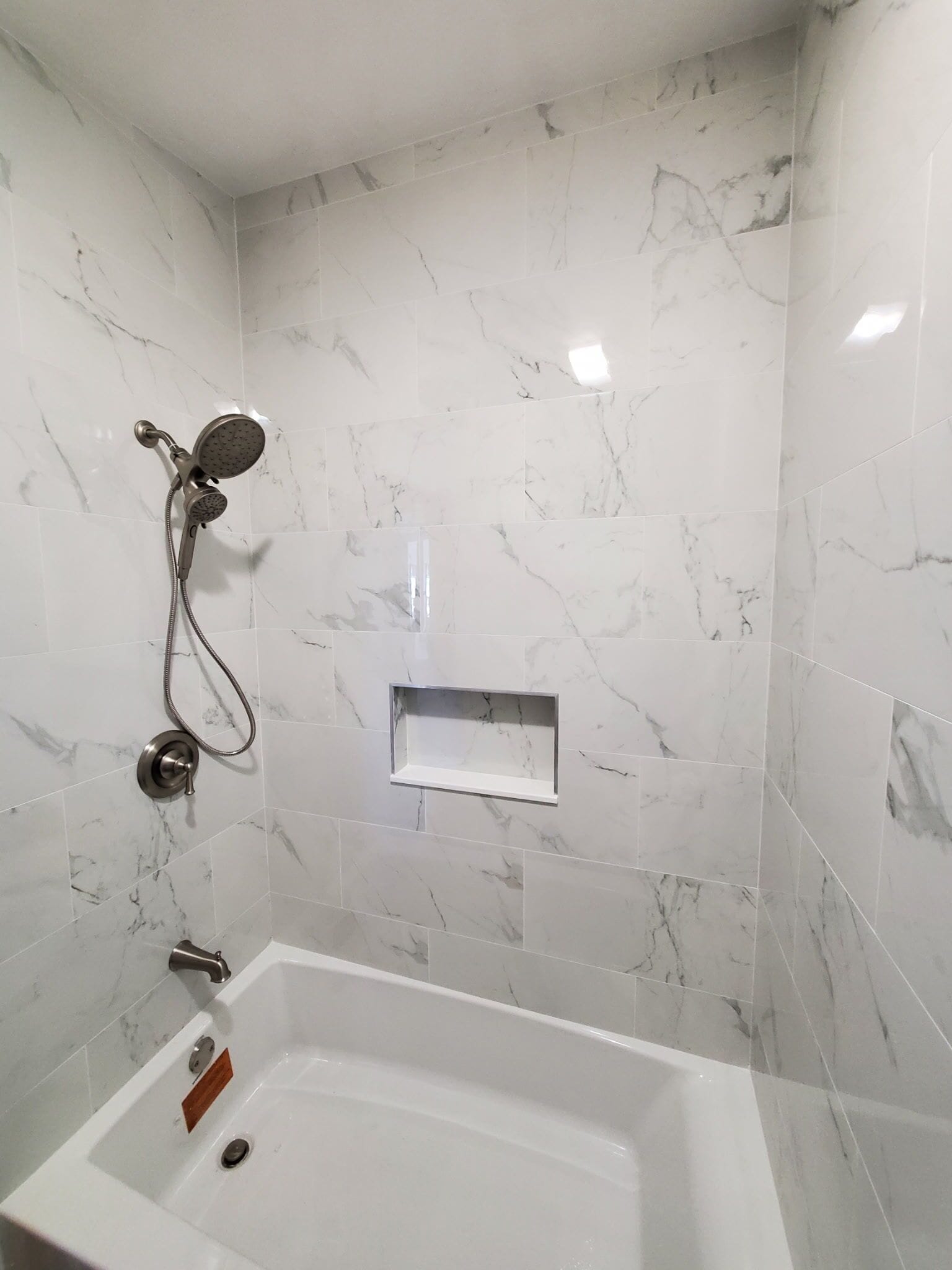 A bathroom with a marble wall, a shower, a bathtub, and a small shelf.