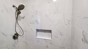 Un baño con pared de mármol, ducha, bañera y un pequeño estante.