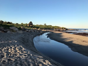 A beach with a calm water body, rocky shoreline, and a distant building. - The Anchor Motel (Narragansett)