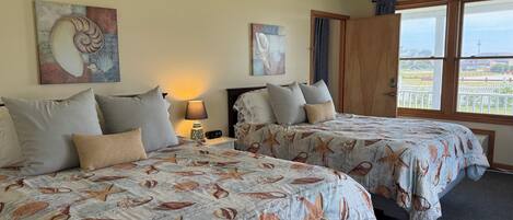 A hotel room with two beds, each with a sea-themed bedspread, a nightstand with a lamp, and artwork on the walls.