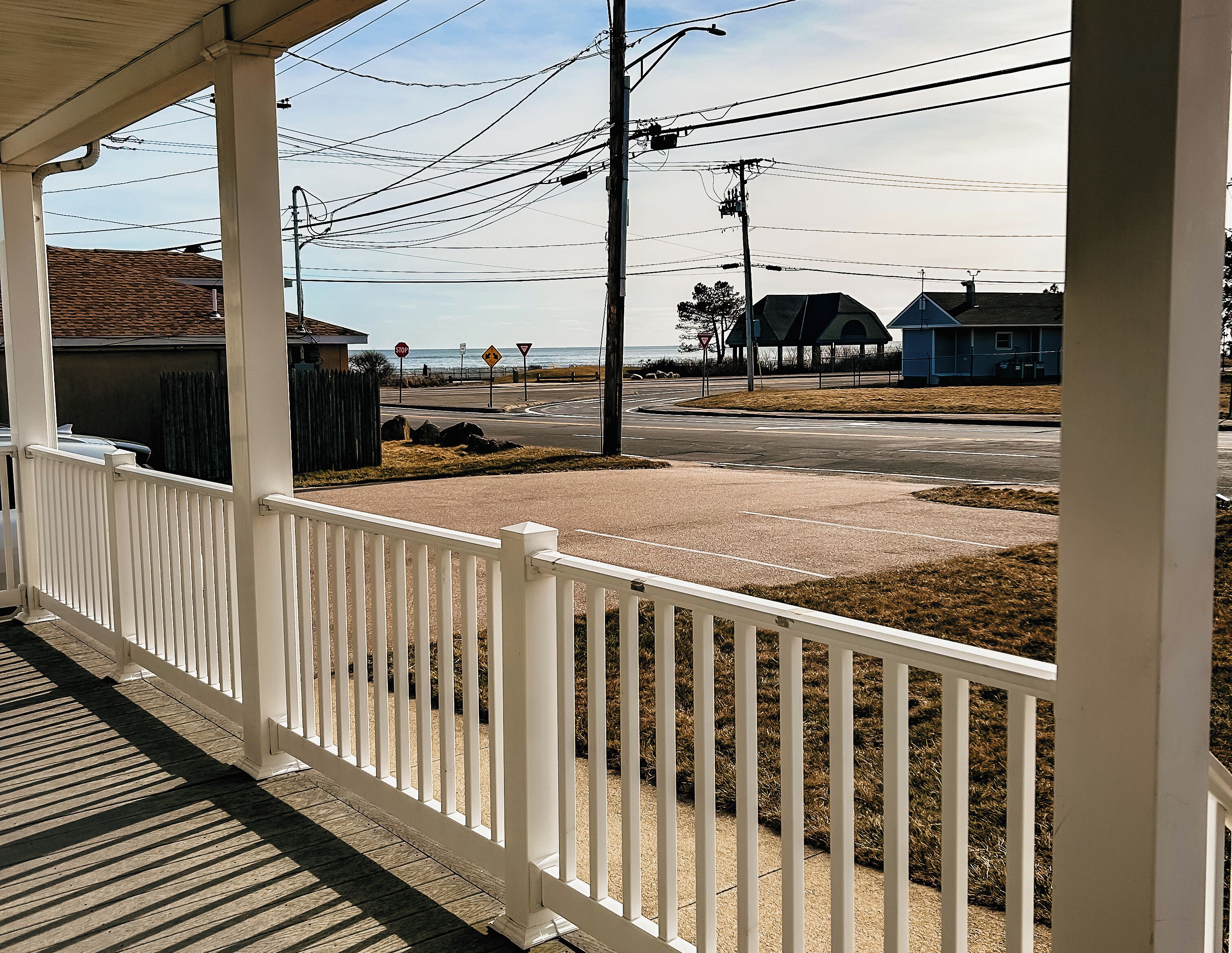 A covered porch with a white railing overlooking a street with a stop sign, a yield sign, and a blue house.