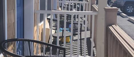 Un espace extérieur abrité, doté d’une terrasse en bois, d’une chaise en métal noir et d’une rambarde blanche.