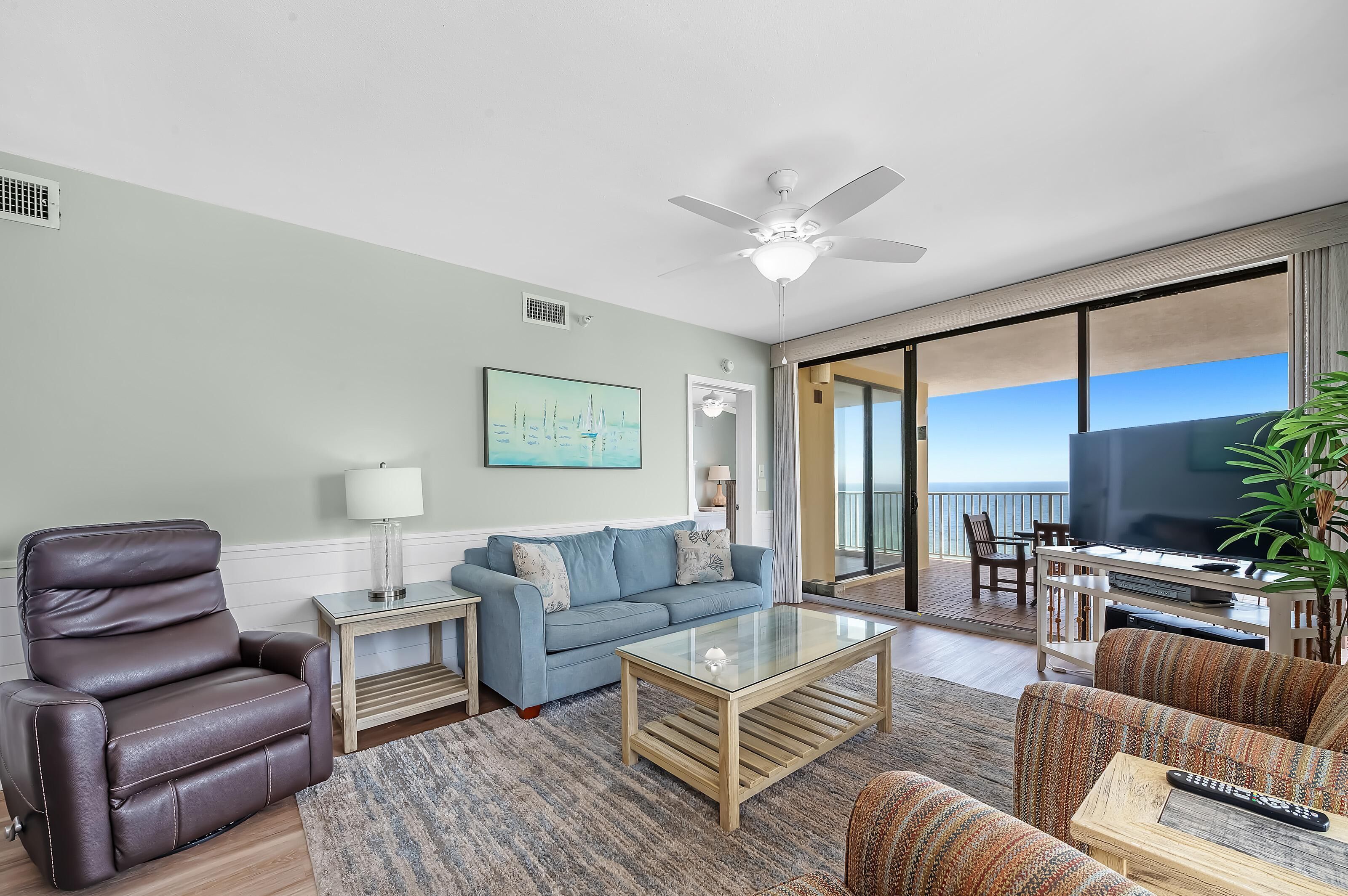 A modern living room with a sofa, a recliner, a coffee table, and a TV area with a balcony view.