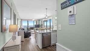 A modern kitchen with a built-in dishwasher, a dining area with a view, and a 'welcome' sign. - Romar Place 1106 (Orange Beach)