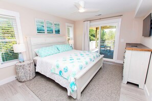 A bedroom with a bed, a bedside table with a lamp, a ceiling fan, and a view of the outdoors. - Oceanside, ELEVATOR, Heated Private Pool, Pool Table, Community Amenities, 713, Sunshine Daydream (Corolla)