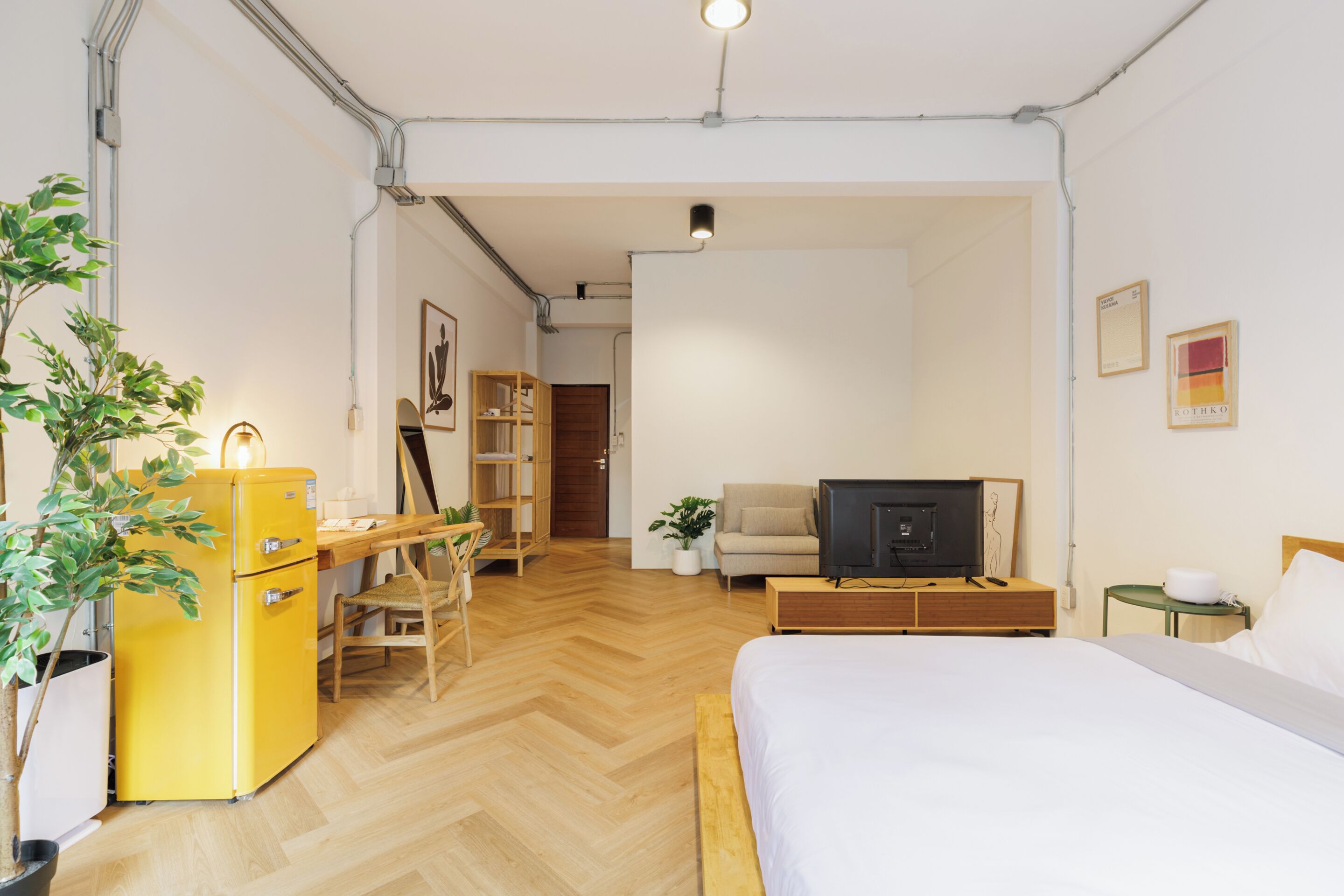 Habitación de hotel con cama, escritorio, silla, televisión, planta y armario.