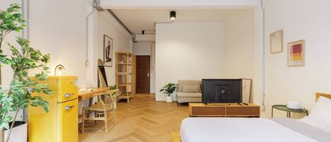 Habitación de hotel con cama, escritorio, silla, televisión, planta y armario.