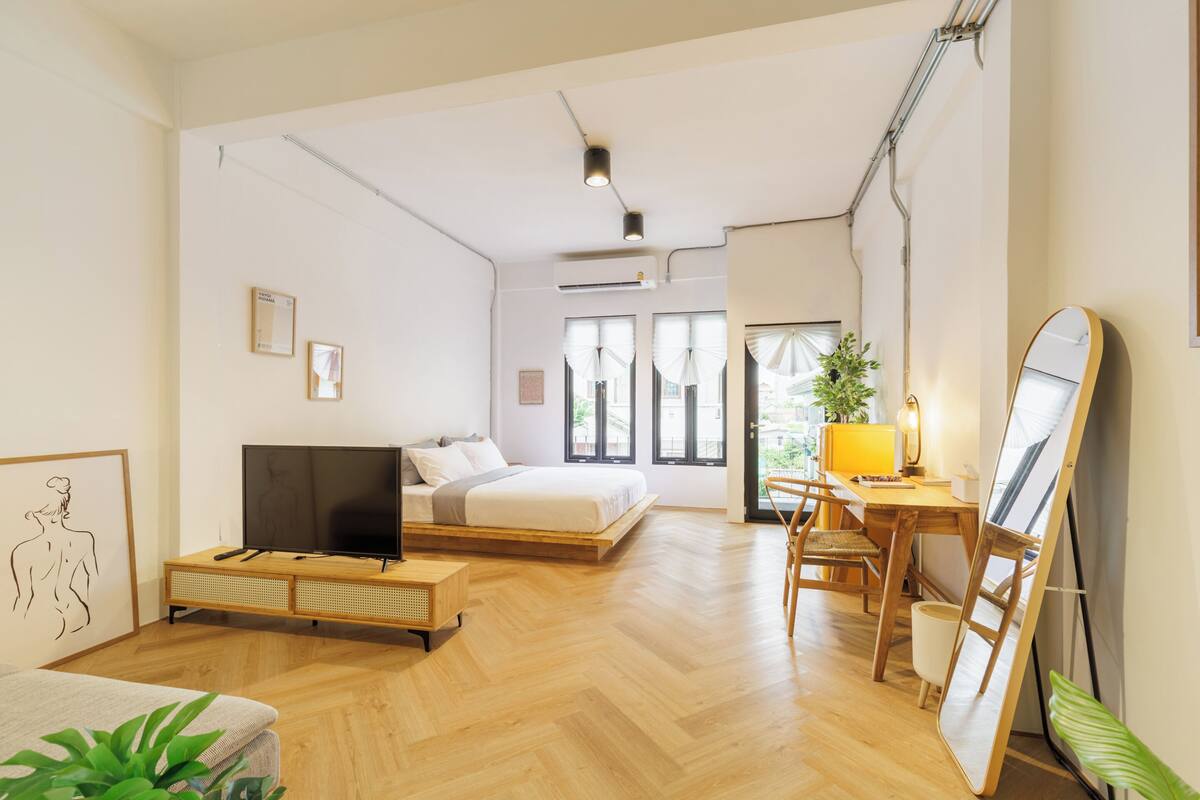 Una habitación amplia con cama, escritorio, televisor y un espejo grande.