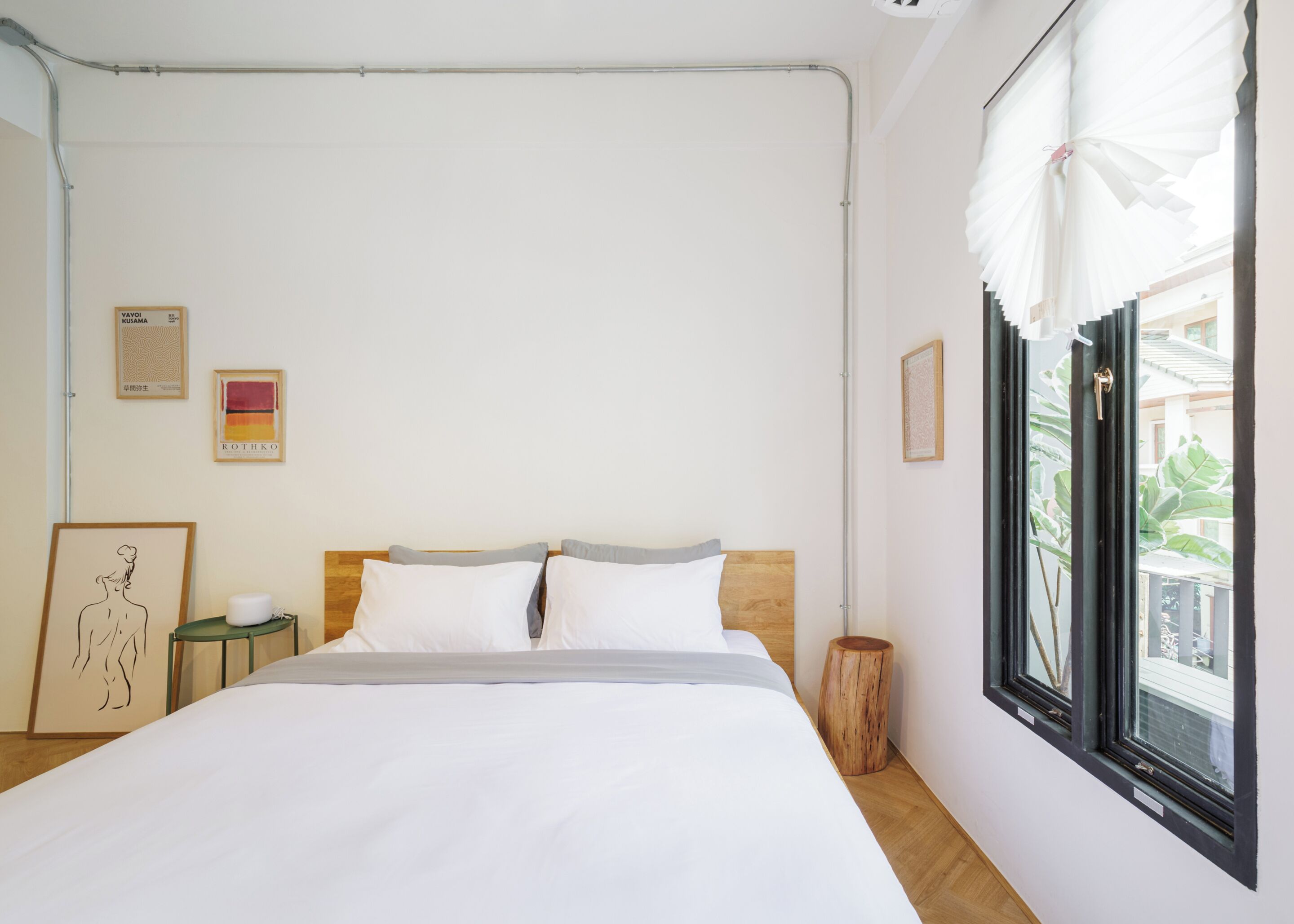 A minimalist bedroom with a wooden headboard, white bedding, and a window with white curtains.