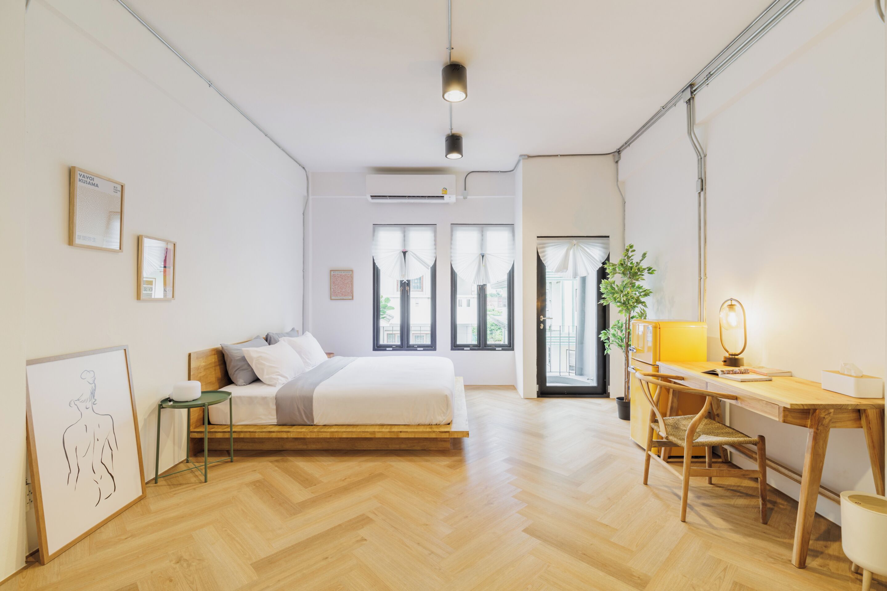 A bedroom with a bed, bedside table, chair, desk, lamp, and a potted plant.