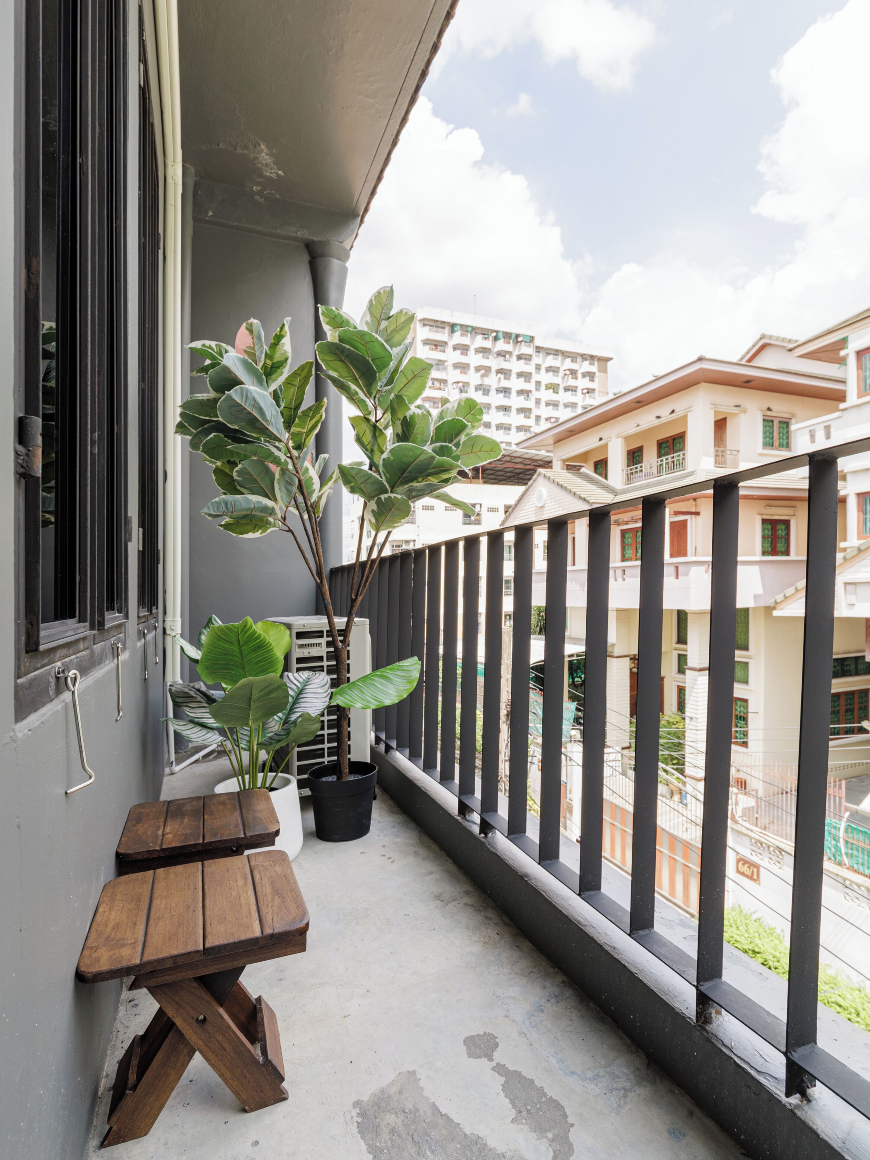 A balcony with a wooden table and potted plants, overlooking a residential area with buildings.