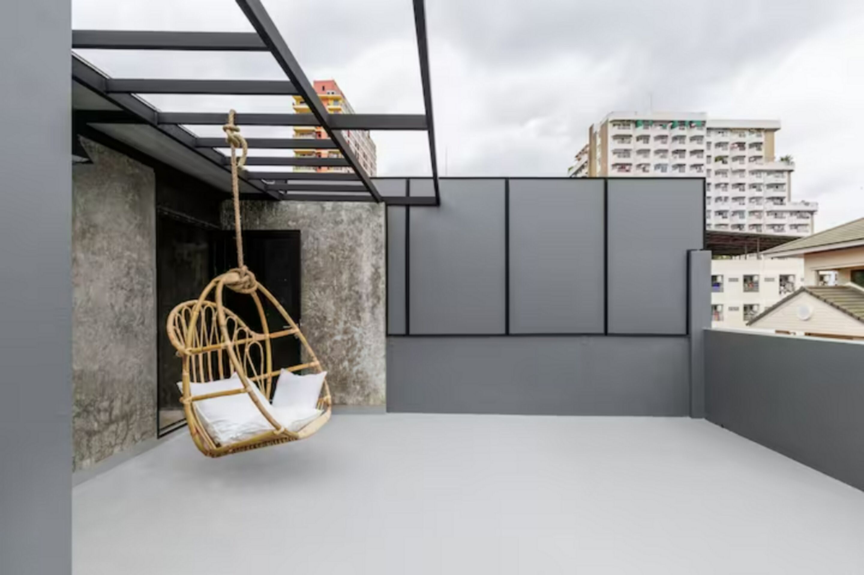 A balcony with a hanging wicker chair, a glass railing, and a view of a building in the background.