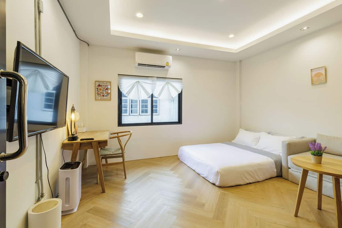 Una habitación de hotel moderna con cama, sofá, escritorio con silla, televisor y aire acondicionado.