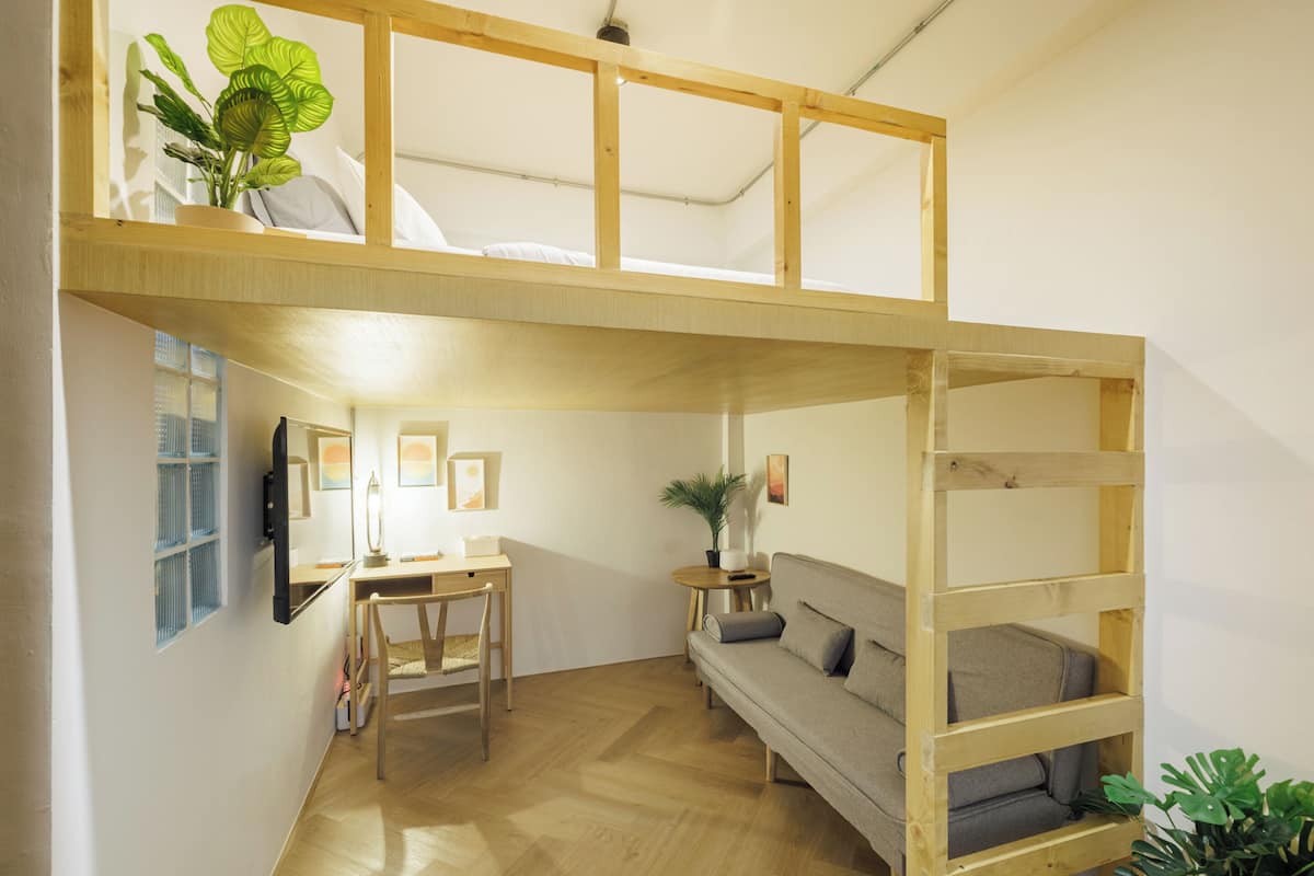 Un cuarto tipo loft con una litera de madera, un sofá, un escritorio y una silla.