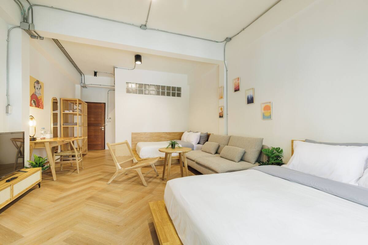 Una habitación de hotel moderna con piso de madera, cama, sofá, escritorio y una silla.