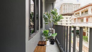Un balcon agrémenté de plantes en pot, d’un banc en bois et offrant une vue sur les bâtiments environnants.