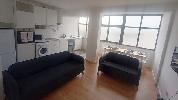 Ein kompakter Wohnraum mit Küchenzeile, einem Essbereich mit Blick und zwei schwarzen Sofas.