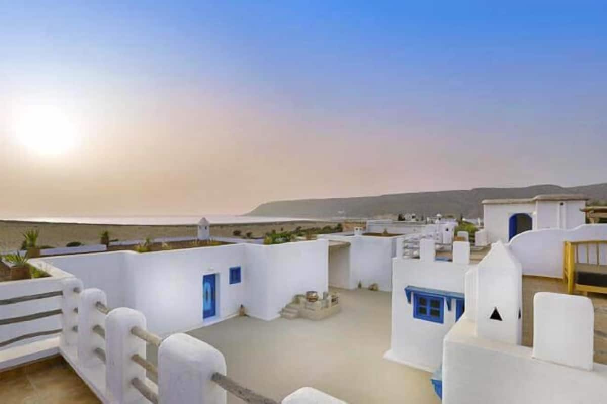 Un edificio costero con paredes blancas y puertas azules, que presenta un techo plano y vistas al mar.