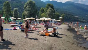 Une plage avec des chaises longues et des parasols, entourée de montagnes et d’arbres.