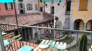 Ein Innenhof mit Terrakotta-Dachziegeln, einem Holztisch mit blauem Kissen und Blick auf angrenzende Gebäude mit Balkonen und Fenstern.