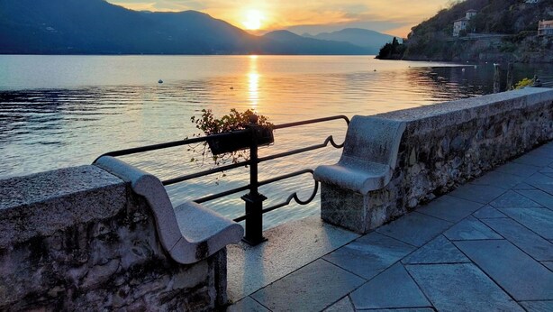 Un banc au bord du lac, doté d’une rambarde en métal, d’où l’on peut admirer un lac paisible avec un coucher de soleil en arrière-plan.