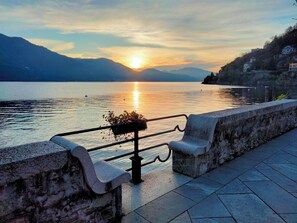 A lakeside bench with a metal railing, overlooking a calm lake with a sunset in the background.