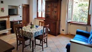 Un coin repas avec une table dressée pour quatre personnes, un téléviseur posé sur une étagère, un meuble avec des portes en verre et une fenêtre donnant sur un paysage verdoyant.