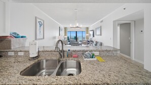 A modern kitchen with granite countertops, stainless steel sink, and a view to the living area. - September Dates Available! Tropical Winds 703! (Gulf Shores)