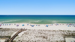 A beach with a wooden boardwalk, sandy beach, and umbrellas. - September Dates Available! Tropical Winds 703! (Gulf Shores)