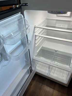 An open refrigerator with clear plastic shelves and a water dispenser.