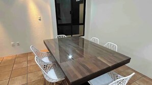 A rectangular dining table with four white chairs, a tiled floor, and a black door in the background.