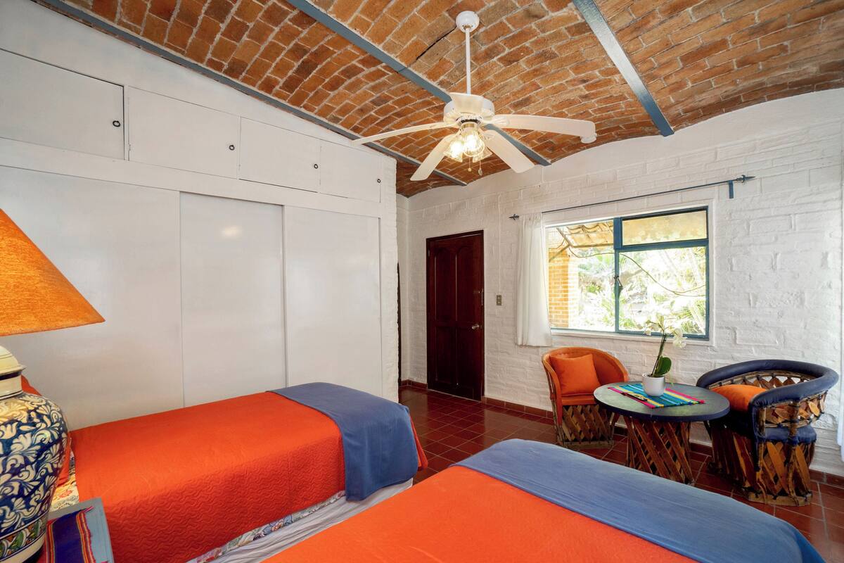 A room with two beds, a ceiling fan, a window with a view, and a table with chairs.