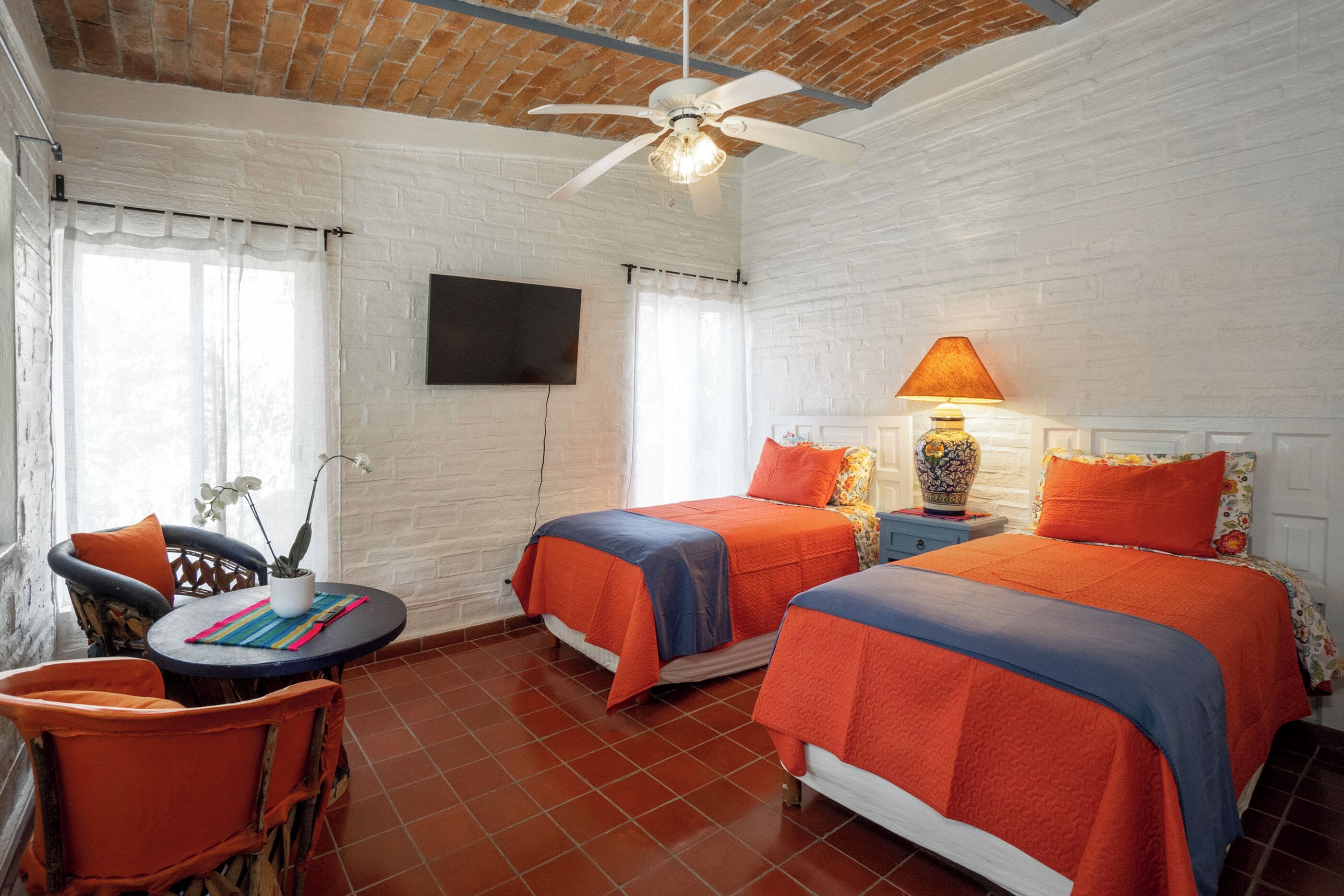 A room with two beds, a ceiling fan, a TV, a table with chairs, and a potted plant.
