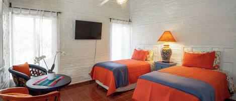 A room with two beds, a ceiling fan, a TV, a table with chairs, and a potted plant.