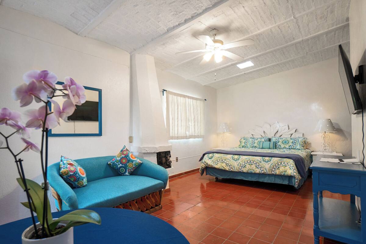 A bedroom with a bed, a blue sofa, a potted orchid, and a ceiling fan.