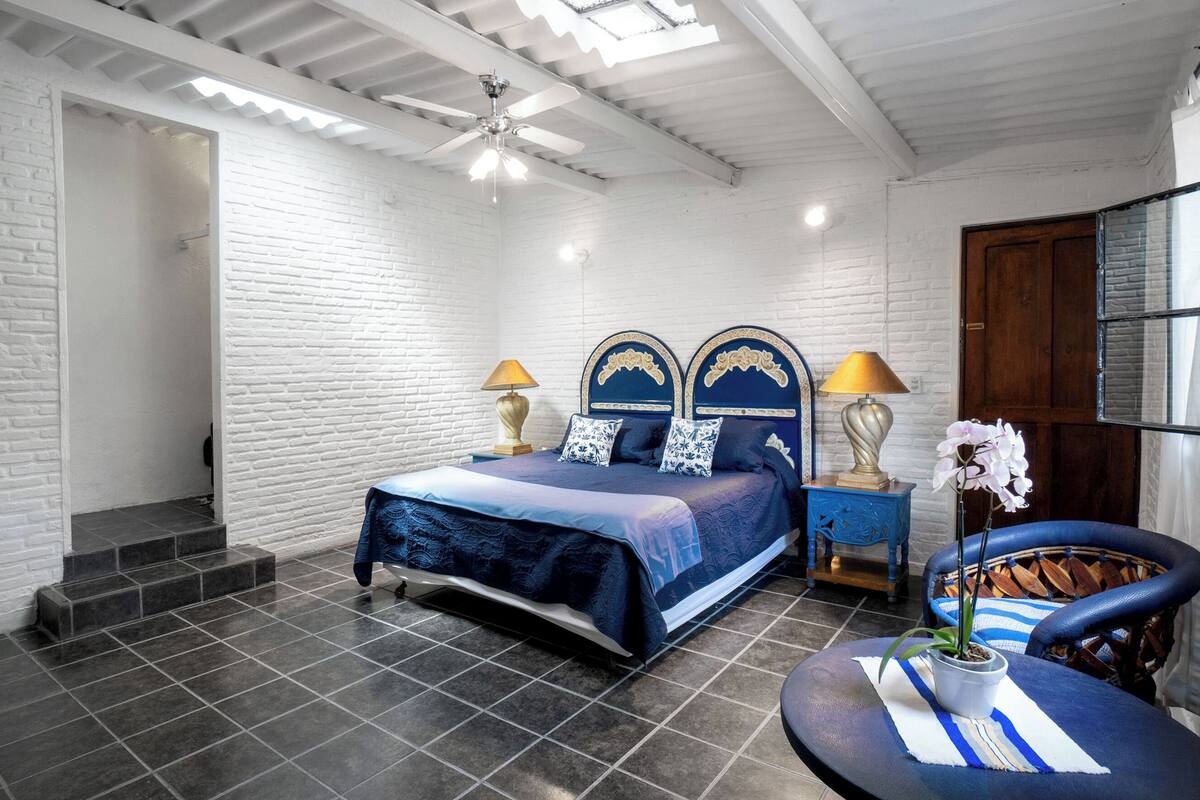 A bedroom with a bed, two bedside lamps, a chair, and a potted orchid.