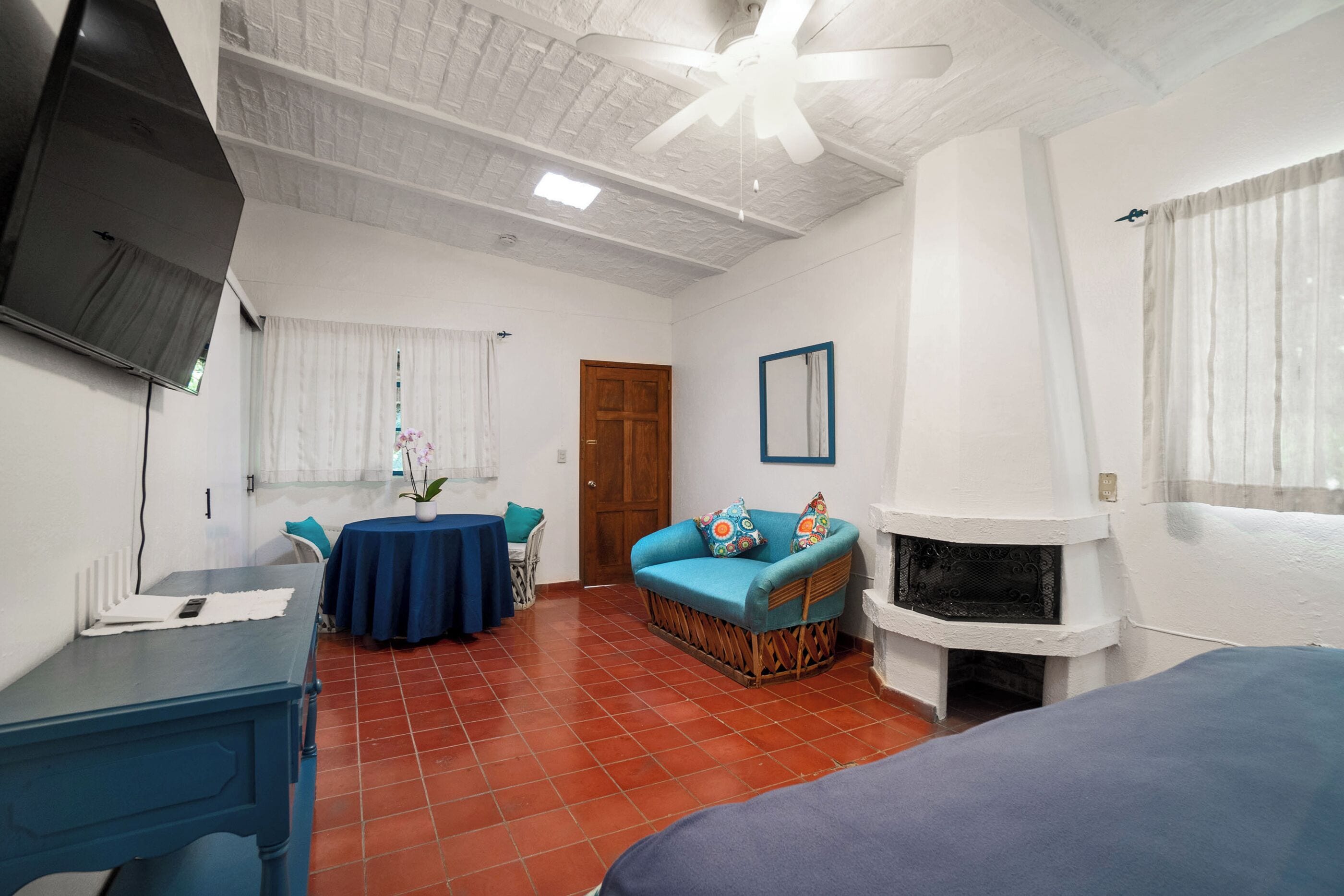 A room with a fireplace, a ceiling fan, a television, a round table with chairs, and a sofa.