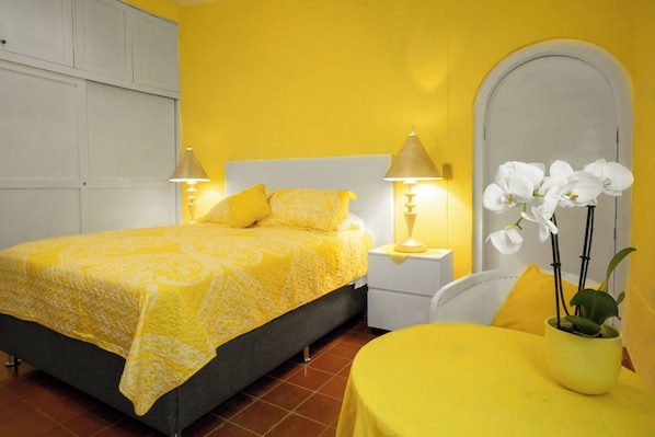 Une chambre avec un lit, deux lampes de chevet, une table de chevet, une chaise et une table sur laquelle est posée une plante en pot.
