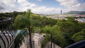 A rooftop terrace with a pool, surrounded by lush greenery and overlooking a cityscape with high-rise buildings. - Morada Pedra Branca  (Balneário Camboriú)