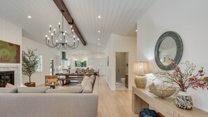 A spacious living room with a large sofa, a chandelier, a fireplace, and a dining area in the background.