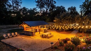 A wooden outdoor kitchen with a barbecue area, surrounded by chairs and a dining table.
