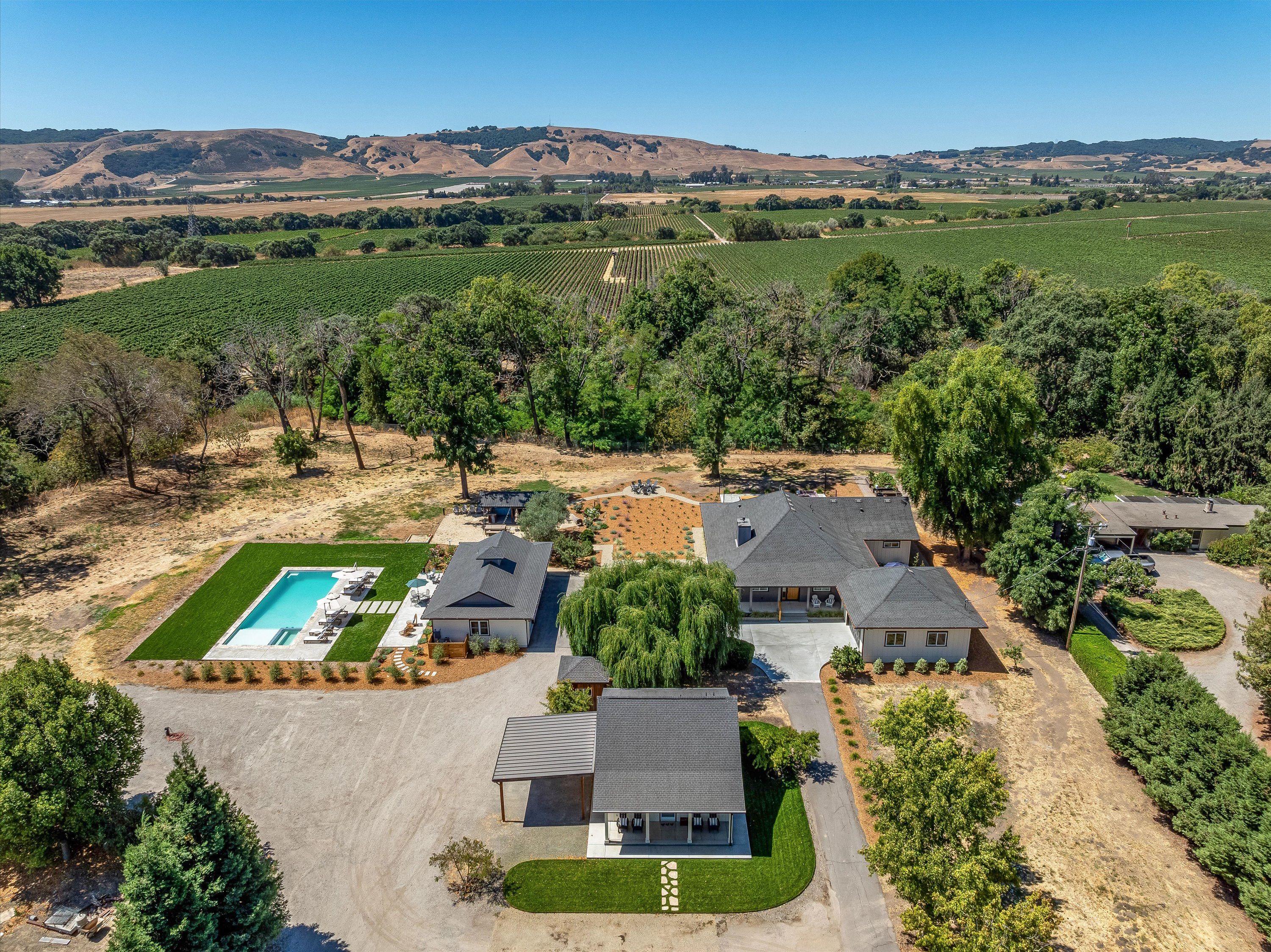 A residential area with multiple houses, a swimming pool, and vineyards in the background.