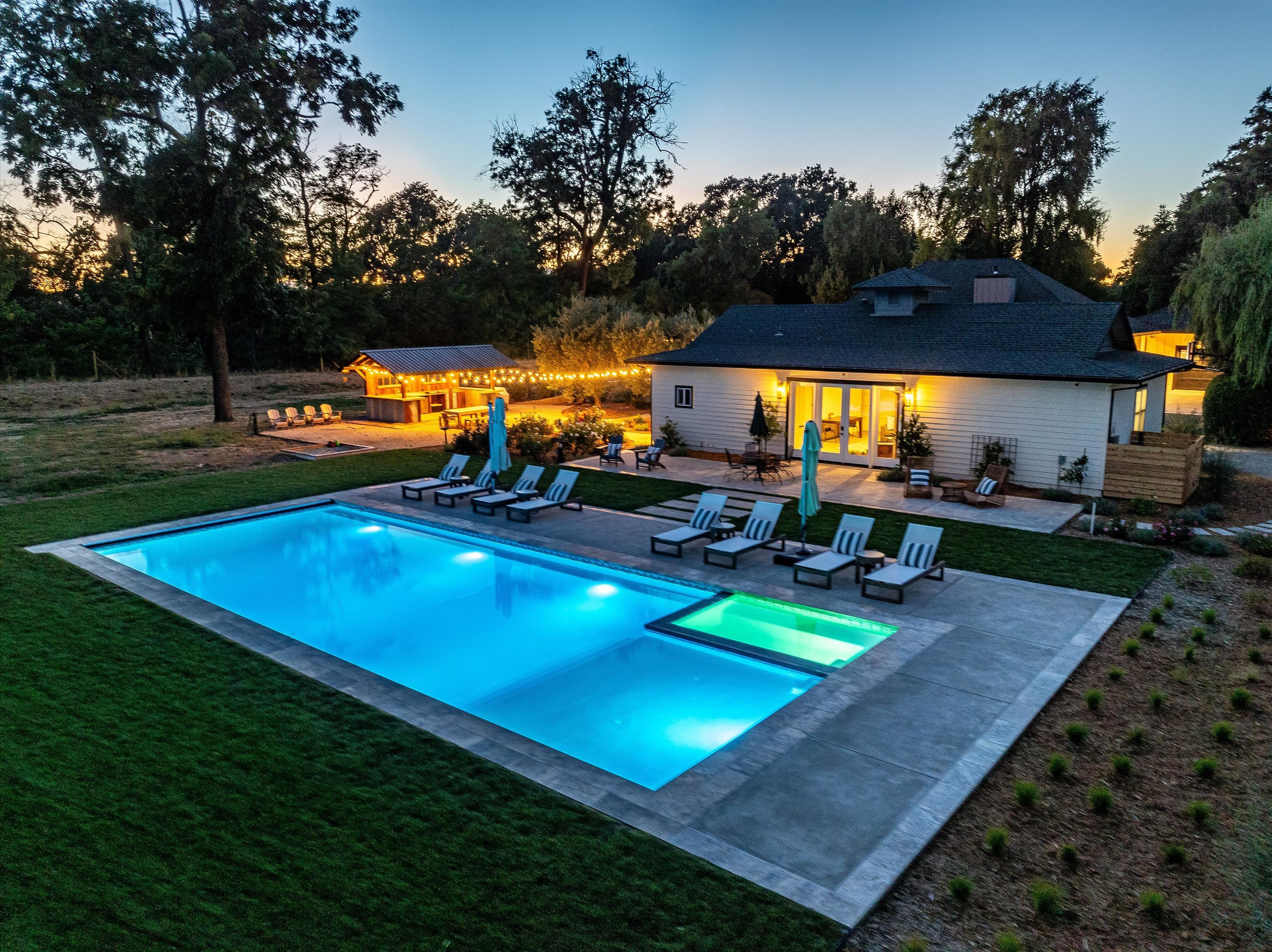 A swimming pool with lounge chairs and a house with outdoor lighting.