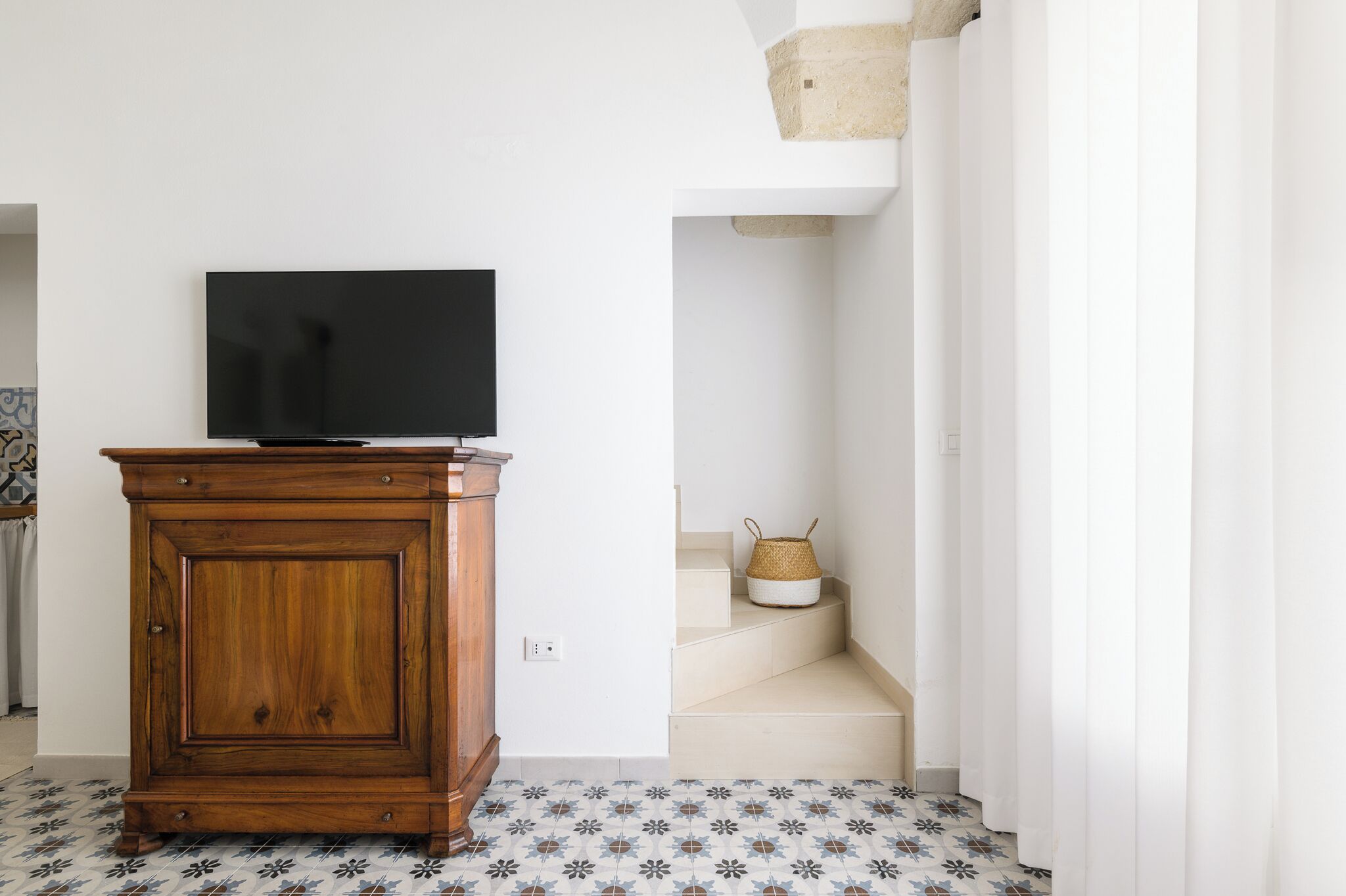 Een houten kast met een televisie erop, een vloer met een patroon en een trap met een mandje op de overloop.